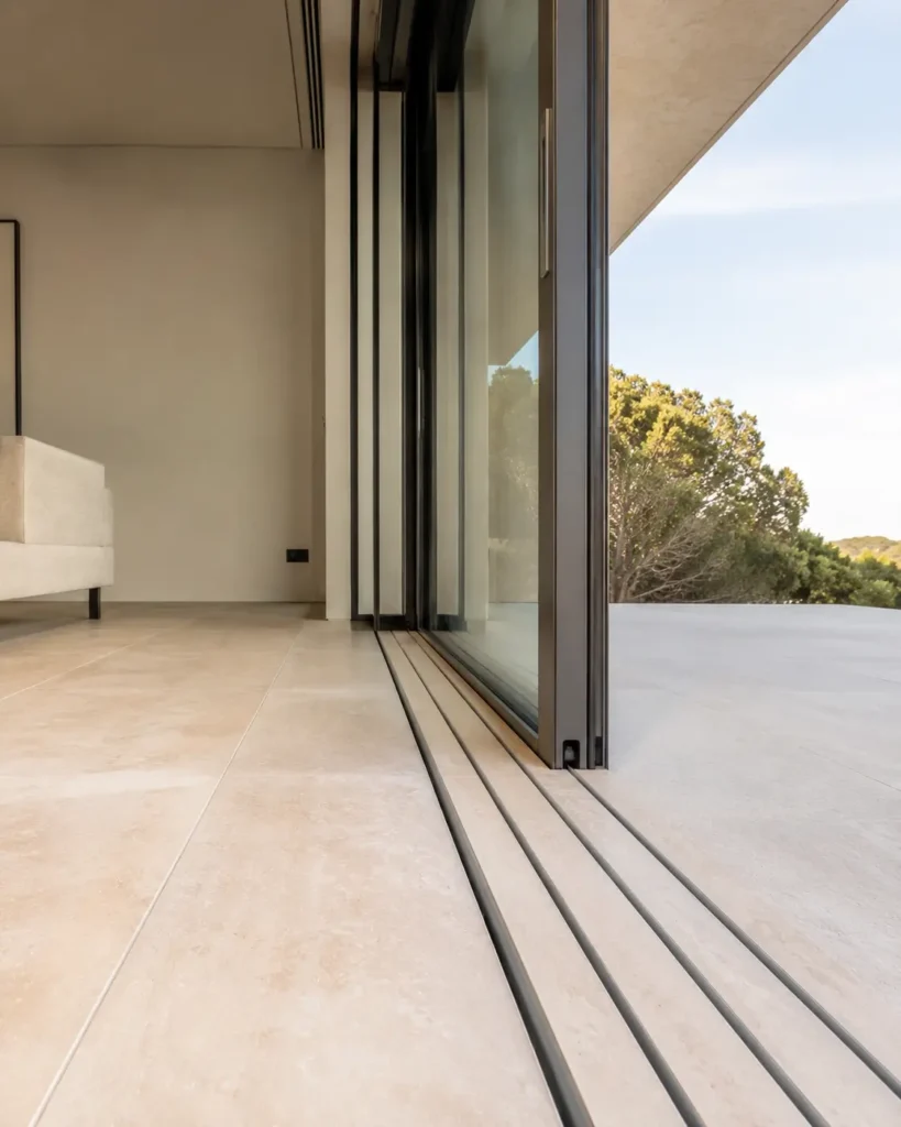 Détail technique d'une baie vitrée minimaliste en aluminium à galandage s'effaçant dans le mur.